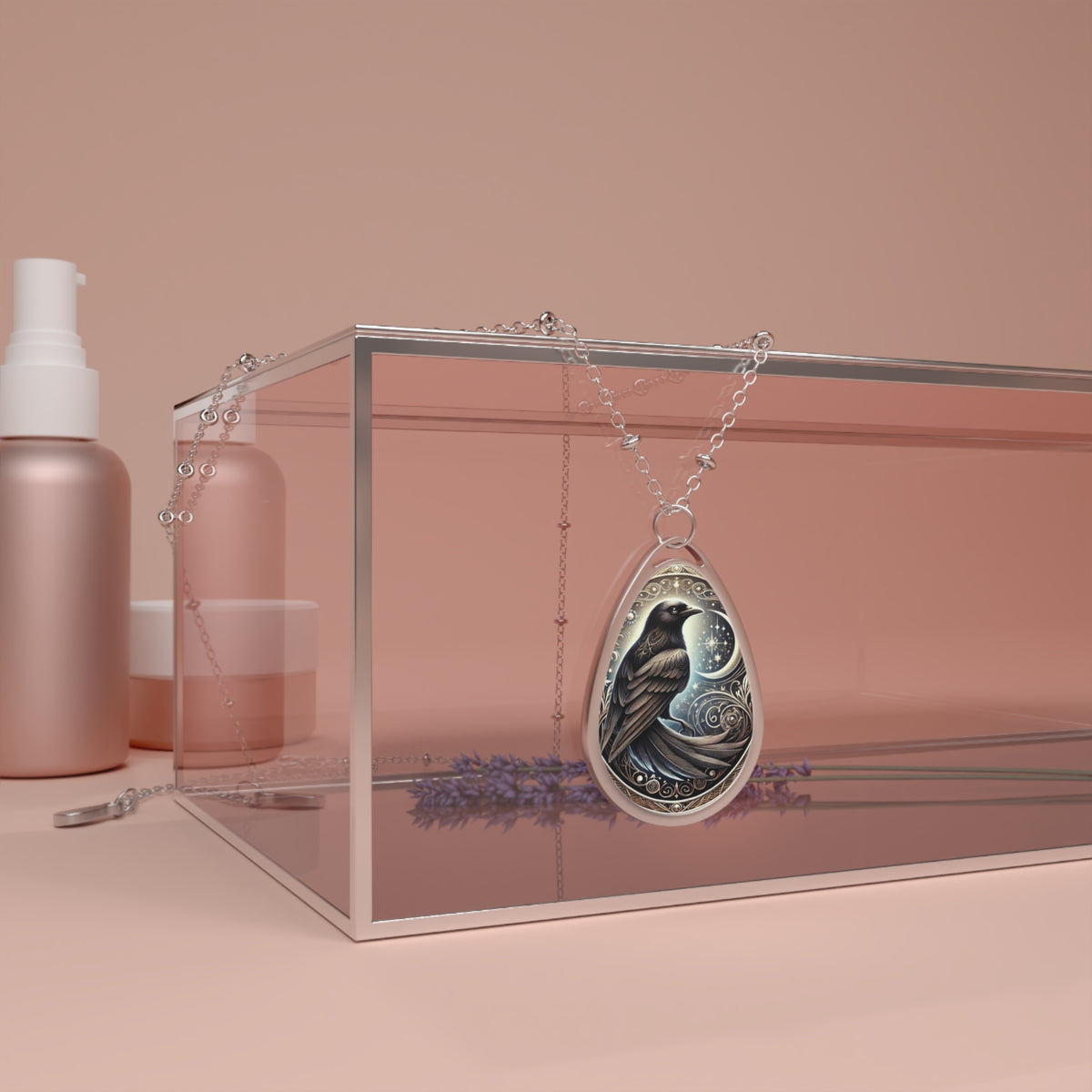 A silver teardrop-shaped necklace pendant featuring an intricately detailed black bird perched under a glowing moon and swirling celestial designs. The pendant hangs from a delicate chain, draped over a clear display box with lavender sprigs nearby.