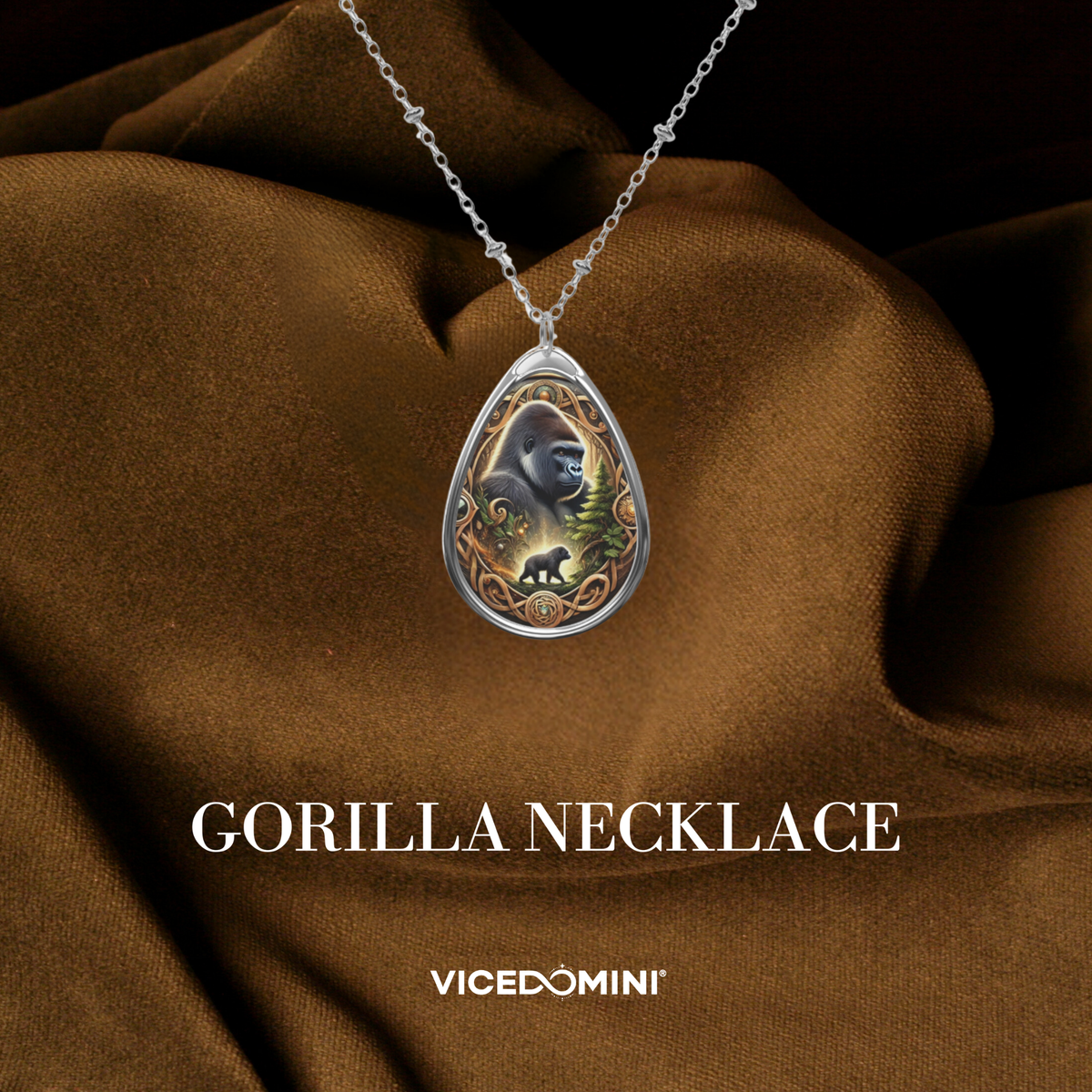 A teardrop-shaped silver pendant necklace featuring an illustrated gorilla and baby gorilla design, displayed on draped brown fabric with the text 'GORILLA NECKLACE' and 'VICEDOMINI' below.