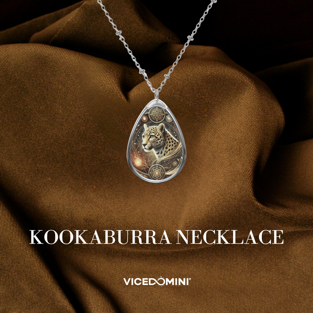 A teardrop-shaped silver pendant necklace featuring an engraved kookaburra bird design, displayed on draped brown fabric with the text 'KOOKABURRA NECKLACE' and 'VICEDOMINI' below.