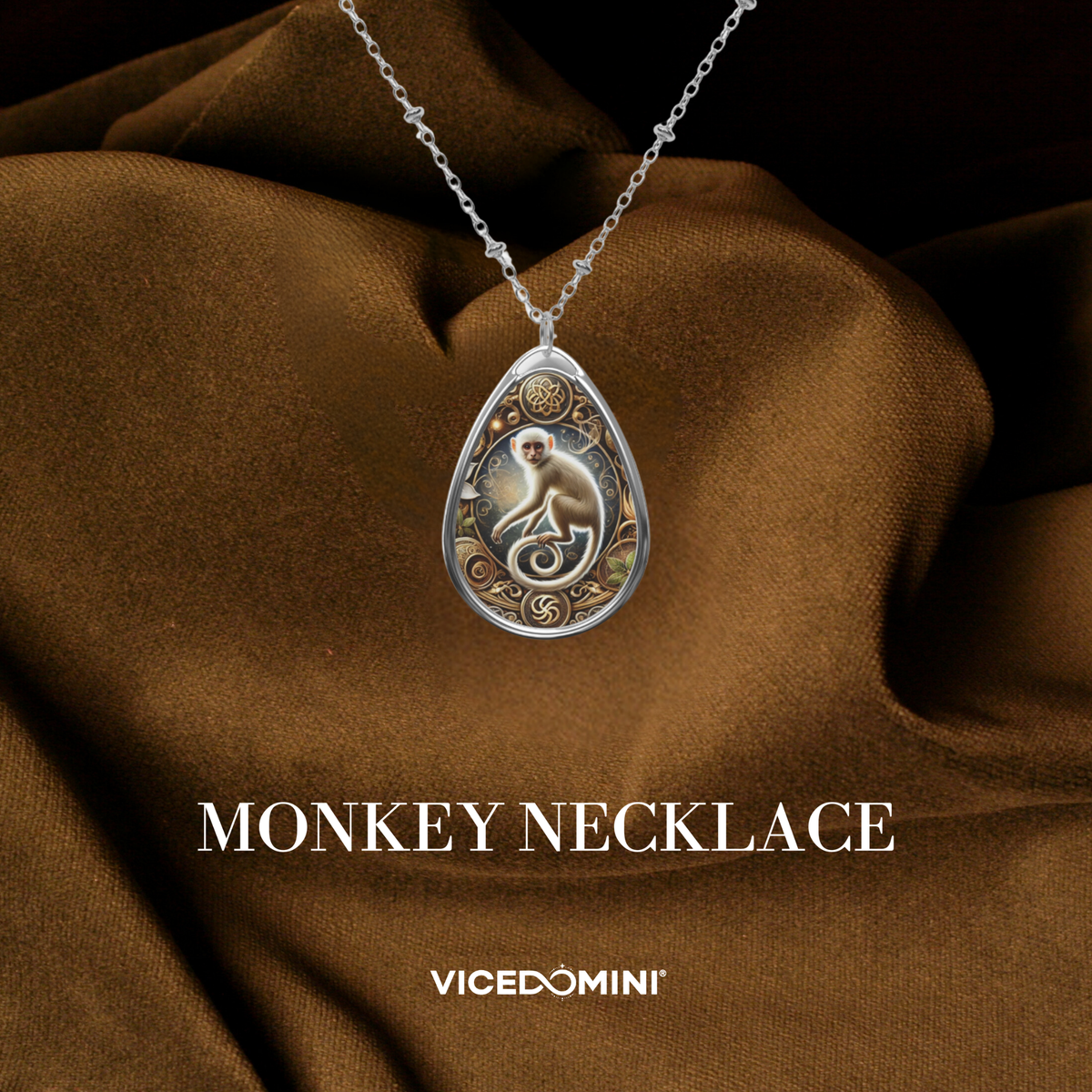 A teardrop-shaped silver pendant necklace featuring an engraved monkey design, displayed on draped brown fabric with the text 'MONKEY NECKLACE' and 'VICEDOMINI' below.