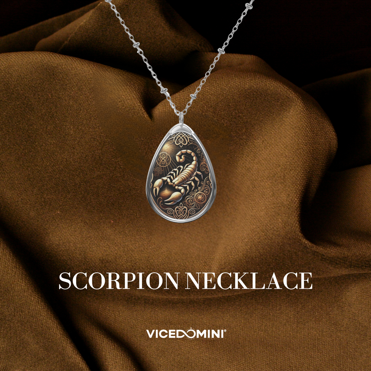 A teardrop-shaped silver pendant necklace featuring an embossed scorpion design in gold and bronze tones, displayed on draped brown fabric with the text 'SCORPION NECKLACE' and 'VICEDOMINI' below.