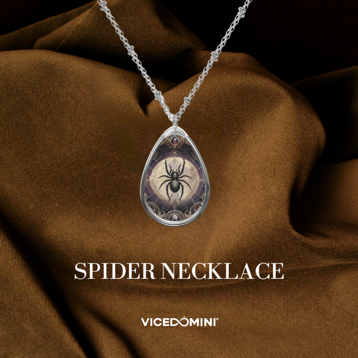 A silver teardrop pendant necklace featuring a spider design over a circular mystical illustration, draped over brown satin fabric with the text 'SPIDER NECKLACE' and 'VICEDOMINI' below.