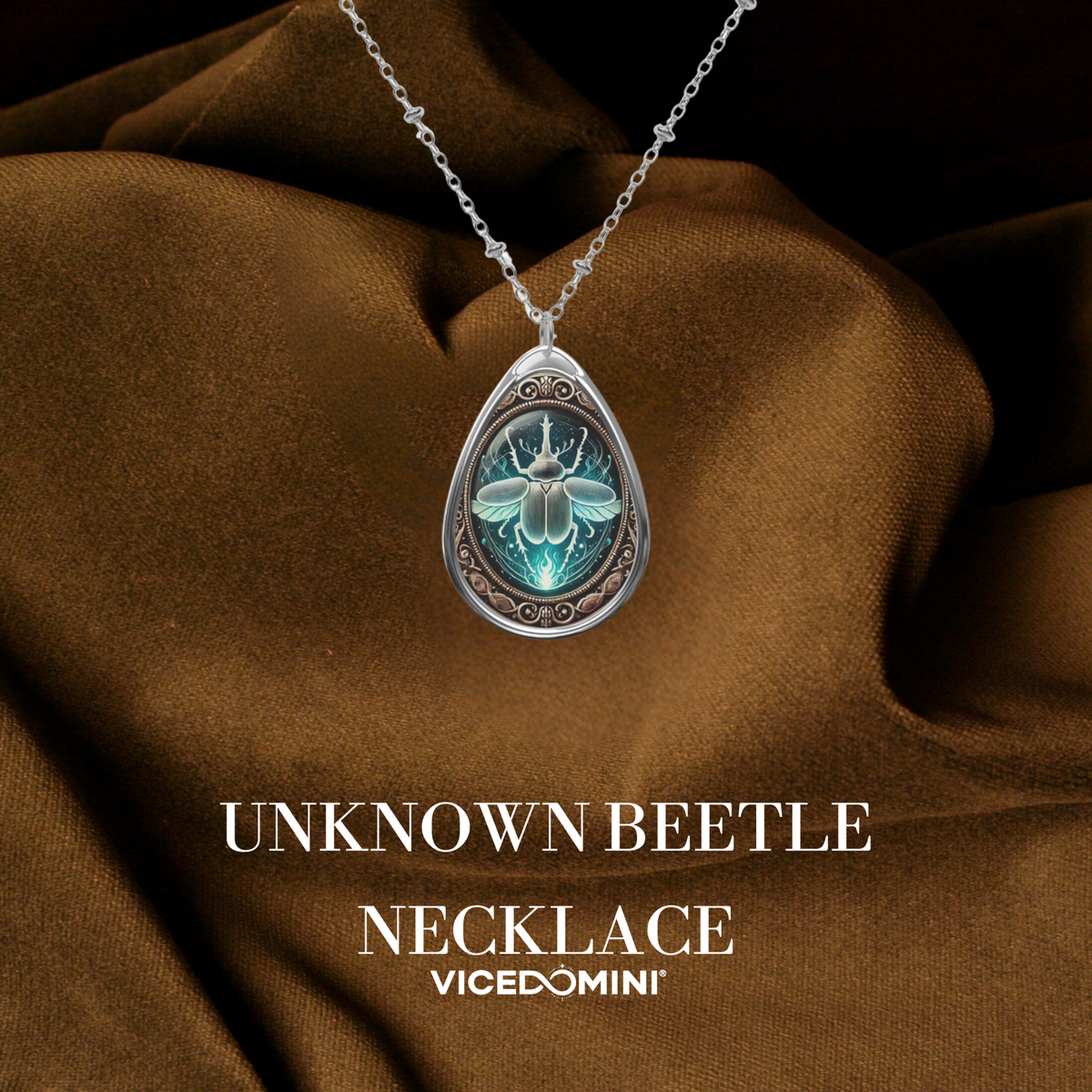 A teardrop-shaped silver pendant necklace featuring an illuminated blue-green beetle design, draped over brown satin fabric with the text 'UNKNOWN BEETLE NECKLACE' and 'VICEDOMINI' below.