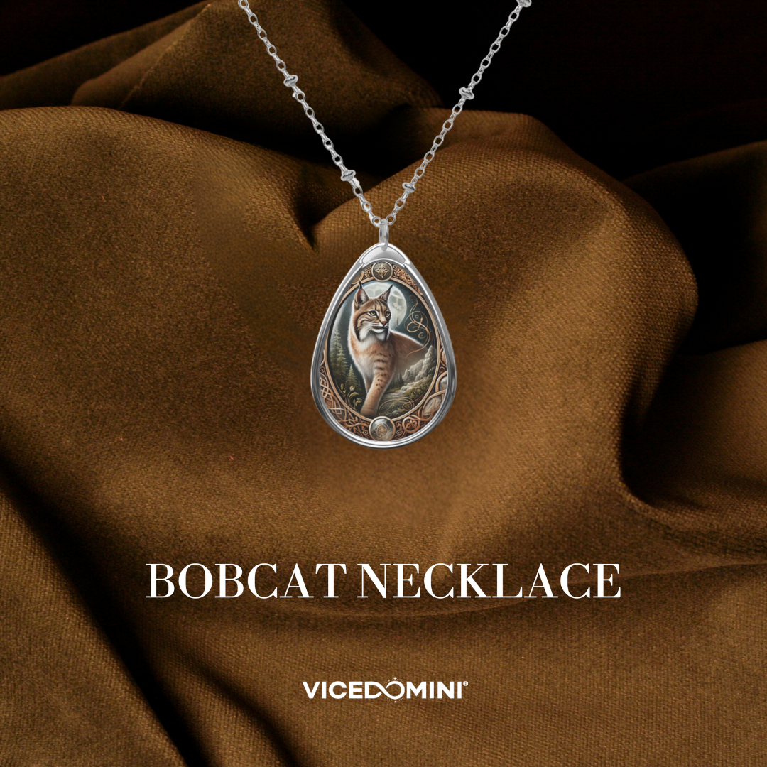 A teardrop-shaped silver pendant necklace featuring an engraved bobcat design, displayed on draped brown fabric with the text 'BOBCAT NECKLACE' and 'VICEDOMINI' below.