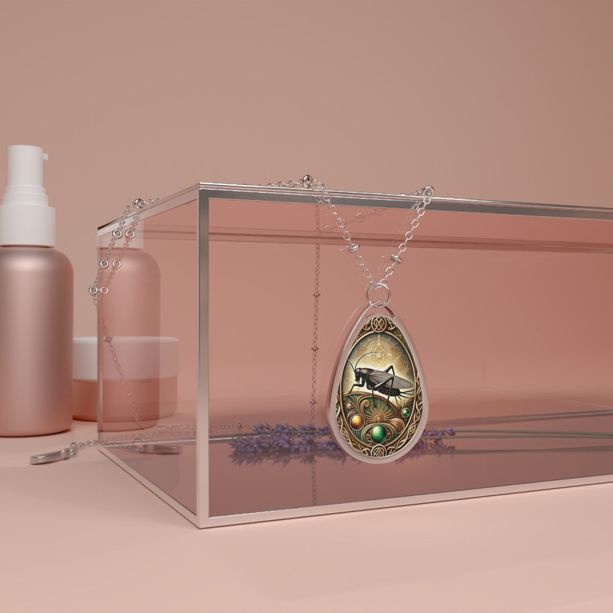 A detailed teardrop-shaped pendant necklace featuring an ornate design with a cricket at its center, resting on a transparent glass box. The background has soft pink tones with lavender sprigs and beauty product bottles, creating a luxurious and elegant setting.