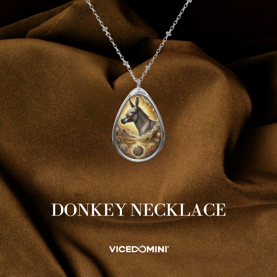 A teardrop-shaped silver pendant necklace featuring an illustrated donkey on a gold-toned background, draped over brown satin fabric. The text 'DONKEY NECKLACE' and the brand 'VICEDOMINI' are displayed below.