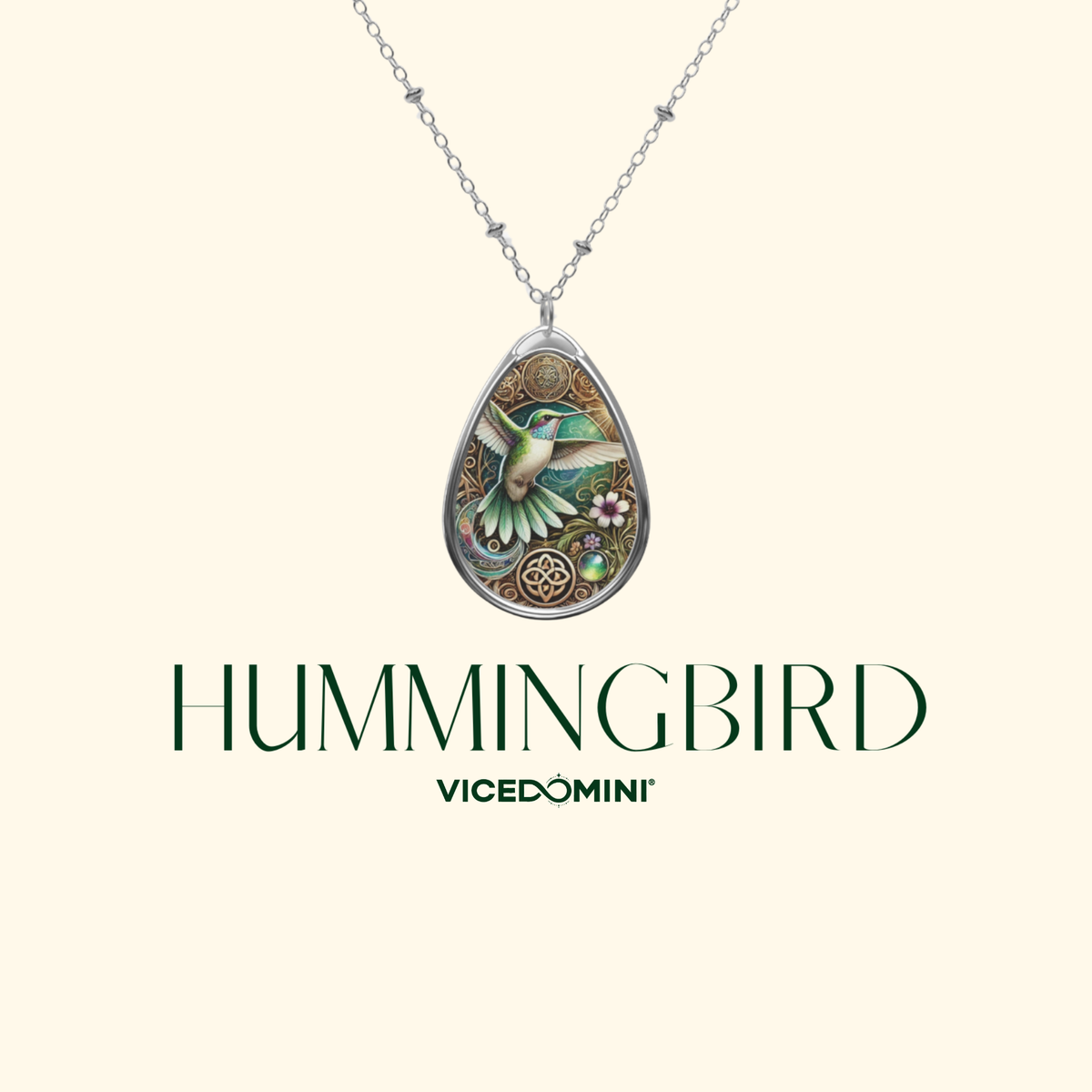 A Vicedomini Hummingbird pendant necklace featuring a detailed hummingbird and floral design in green, gold, and silver, suspended from a delicate silver chain against a light cream background with the brand name displayed below.