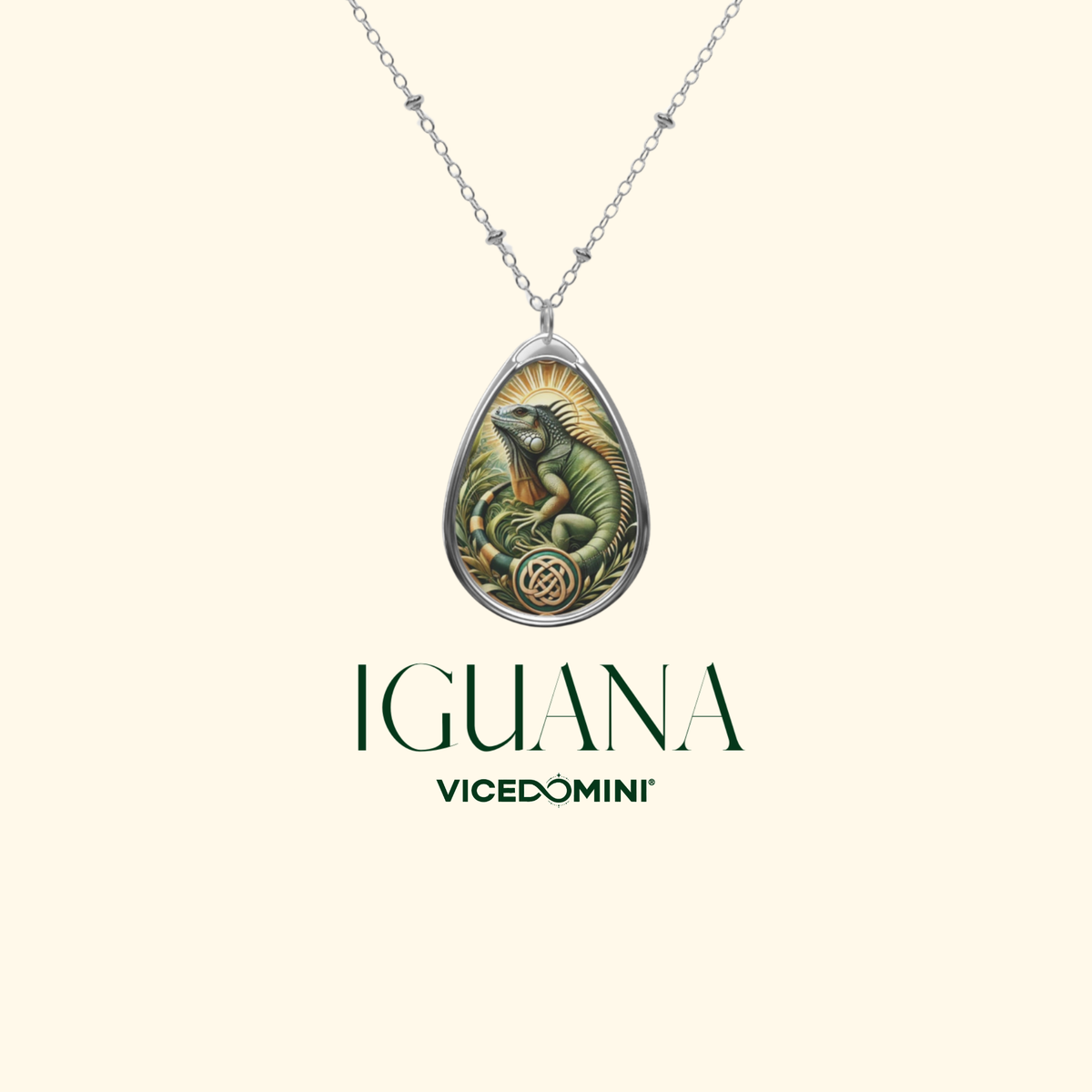 A silver teardrop pendant necklace featuring an illustrated green iguana and a gold sunburst, displayed on a cream background with the brand name 'IGUANA VICEDOMINI' below.