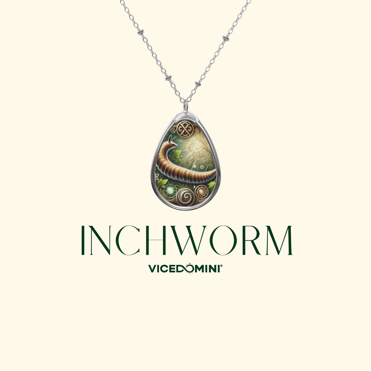 A teardrop-shaped pendant necklace featuring a detailed illustration of a brown worm wrapped in green leaves and gold-toned spiral details, suspended from a silver chain. The brand name 'Vicedomini' and the product name 'INCHWORM' are displayed below the necklace on a solid pale cream background.