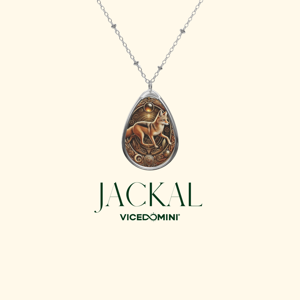 A teardrop-shaped pendant necklace featuring an intricate illustration of a jackal with a golden sun and moon, suspended from a silver chain. The brand name 'JACKAL' and sub-brand 'VICEDOMINI' are displayed below the pendant on a solid cream-colored background.