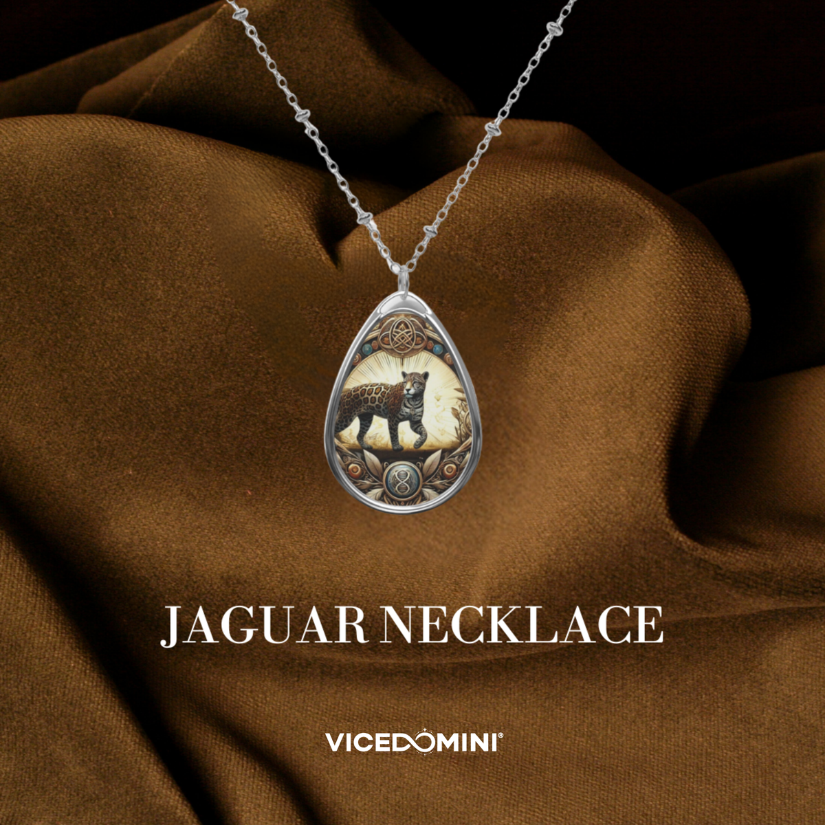 A teardrop-shaped silver pendant necklace featuring an engraved or printed jaguar design, displayed on draped brown fabric with the text 'JAGUAR NECKLACE' and 'VICEDOMINI' below.