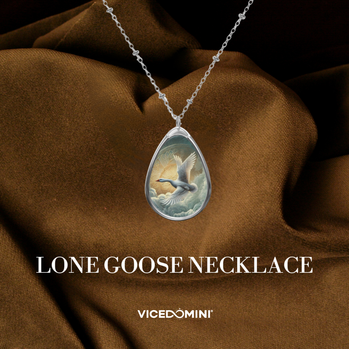 A teardrop-shaped pendant necklace with a silver-toned chain, featuring a detailed illustration of a lone goose flying over clouds. The pendant is displayed against a draped brown fabric background with the text 'LONE GOOSE NECKLACE' and the brand 'VICEDOMINI' below.