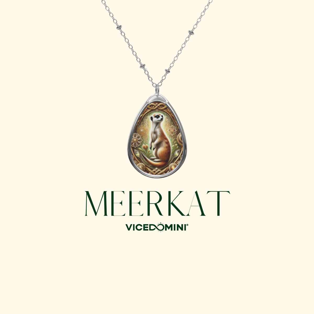 A teardrop-shaped silver pendant necklace featuring an illustrated meerkat, suspended from a delicate silver chain against a light cream background. Below the necklace, the text 'MEERKAT' and 'VICEDOMINI' are displayed in dark green.
