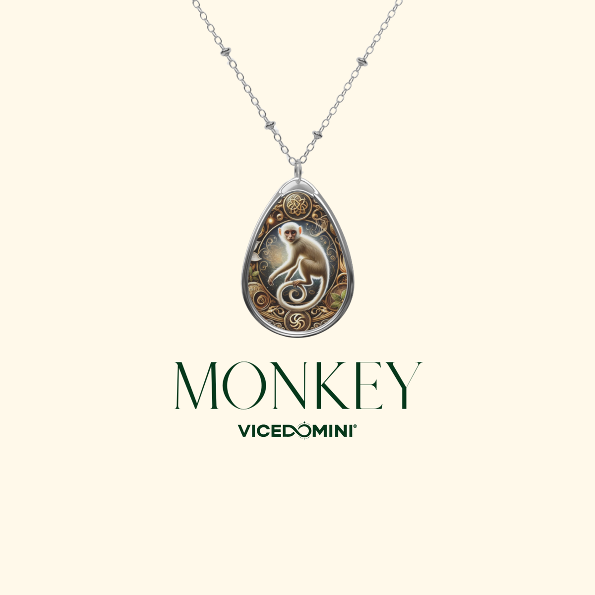 A silver teardrop pendant necklace featuring an engraved monkey illustration and ornate detailing, suspended from a delicate silver chain against a light cream background. Below the necklace, the brand name 'VICEDOMINI' and the word 'MONKEY' are printed in dark green.