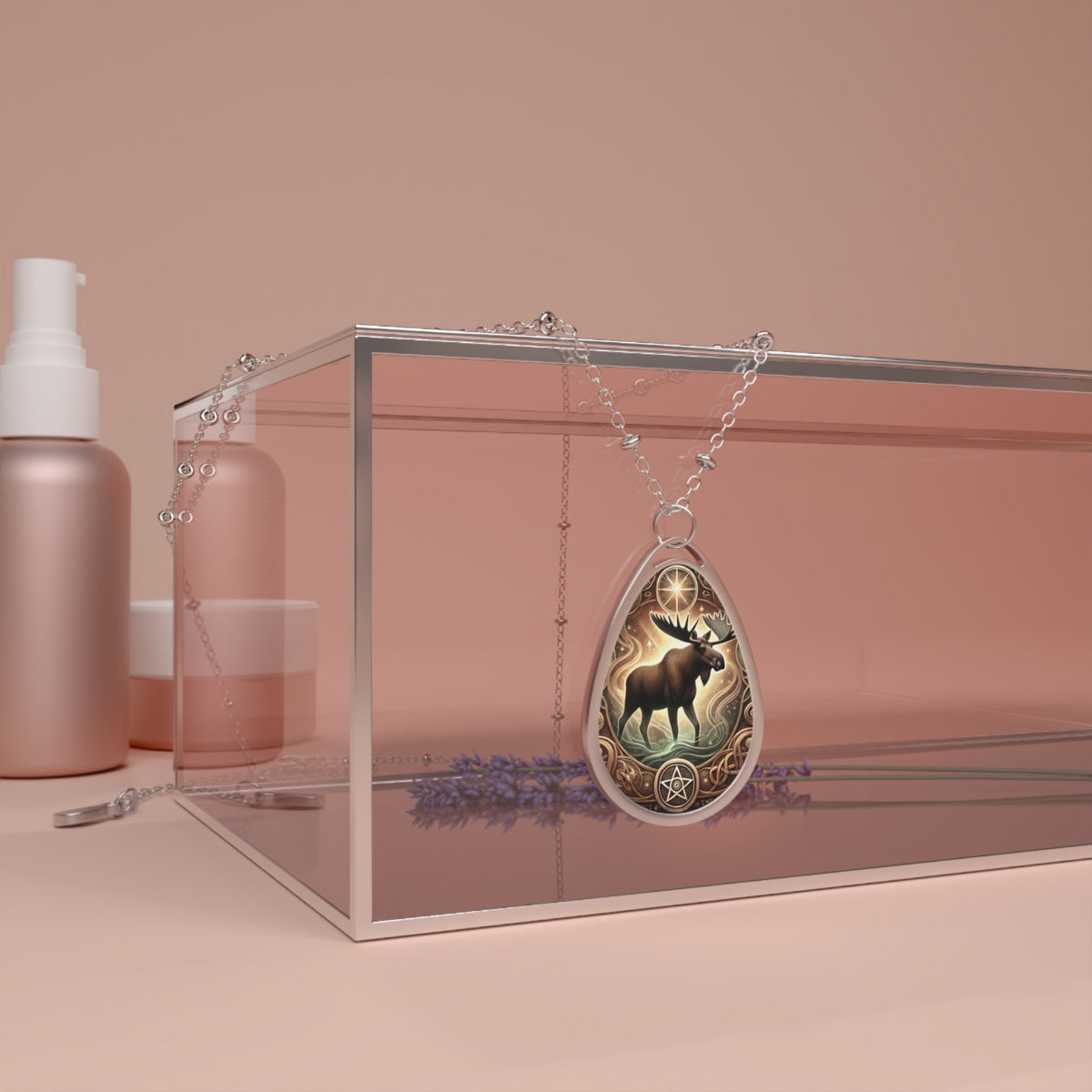 The moose pendant necklace elegantly drapes over a transparent glass box, with soft pink and lavender accents in the background. The pendant features an artistic moose motif with golden celestial elements, creating a mystical aesthetic.