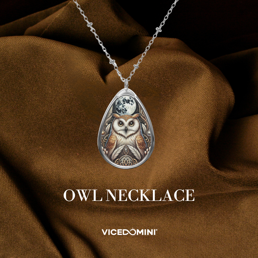 A silver owl pendant necklace with an intricate owl illustration and moon design, draped over brown satin fabric. The text 'OWL NECKLACE' and 'VICEDOMINI' are displayed below the necklace.
