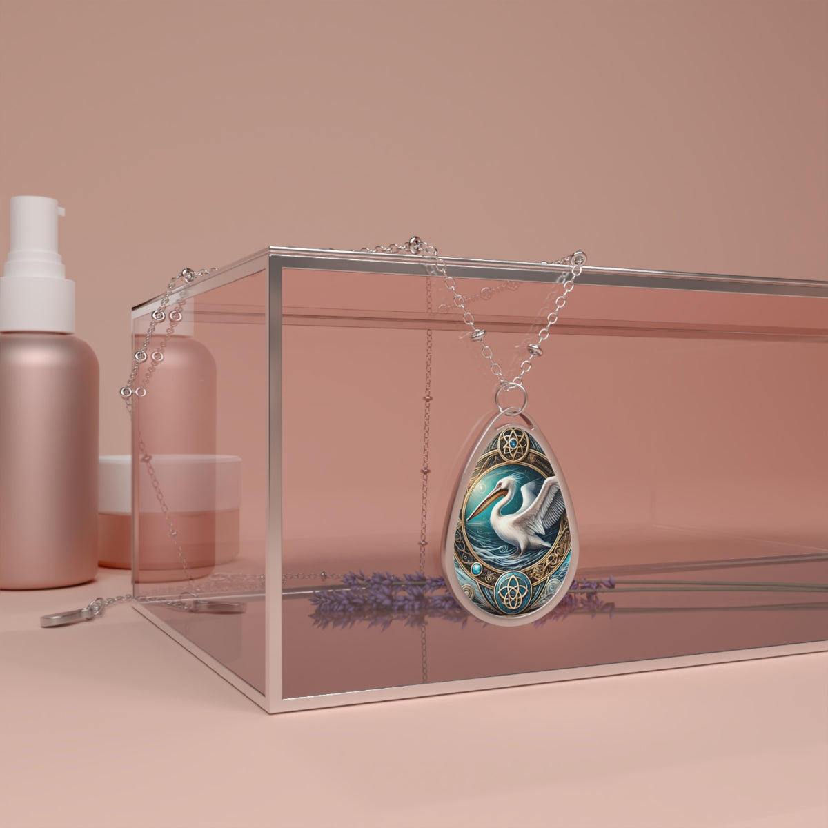 A pelican-themed pendant with intricate gold and blue detailing draped over a clear jewelry display box, placed on a pastel pink surface with a lavender sprig beside it. The pendant exudes elegance and craftsmanship.