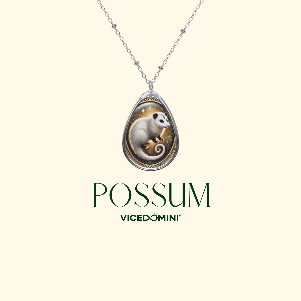 A silver-toned teardrop pendant necklace featuring an illustrated white possum on a warm gold and brown background, shown on a light cream backdrop with the text 'POSSUM VICEDOMINI' below.