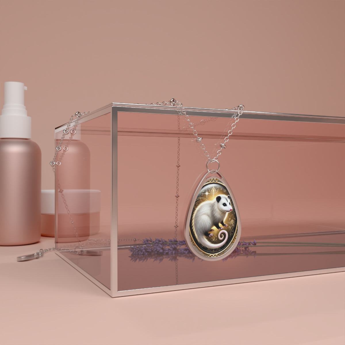 A close-up of the possum pendant resting against a transparent jewelry box with a blush-toned backdrop. The pendant's silver frame holds an artistic rendering of a possum with golden floral and swirling elements surrounding it. The setting includes subtle lavender and skincare products for an aesthetic touch.