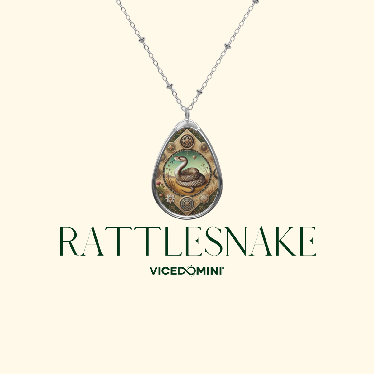 A silver teardrop pendant necklace featuring an illustrated rattlesnake design, displayed against a light cream background with the text 'RATTLESNAKE' and 'VICEDOMINI' below.