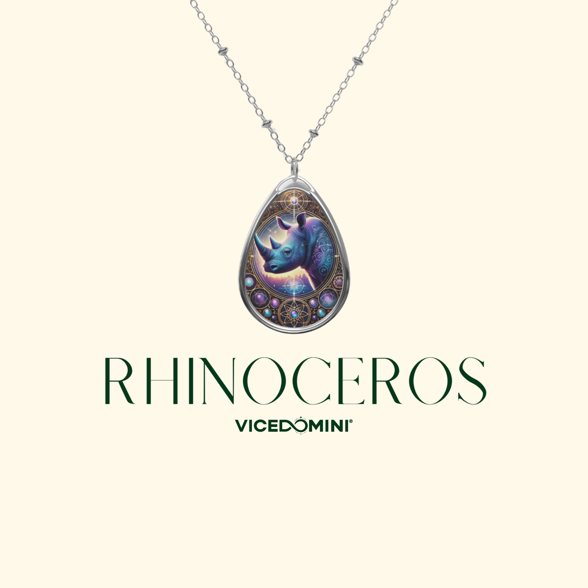 Close-up of a silver rhinoceros pendant necklace suspended on a delicate chain, set against a clean cream-colored background. The pendant showcases a cosmic-inspired design with glowing purple tones and celestial details, labeled "Rhinoceros - VICEDOMINI."