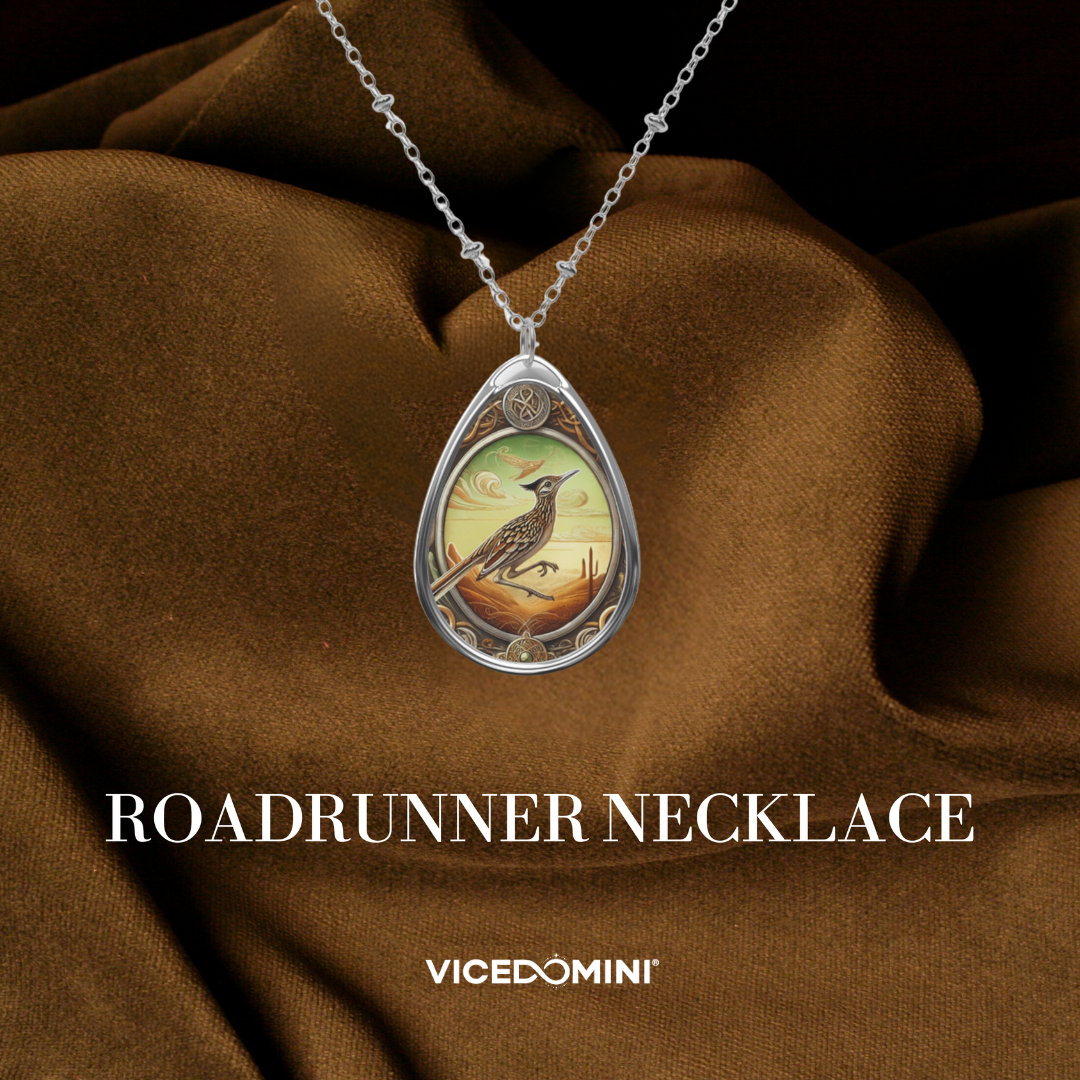 A teardrop-shaped silver pendant necklace featuring an illustrated bird scene, displayed on draped brown satin fabric. The text 'ROADRUNNER NECKLACE' and 'VICEDOMINI' are overlaid at the bottom.
