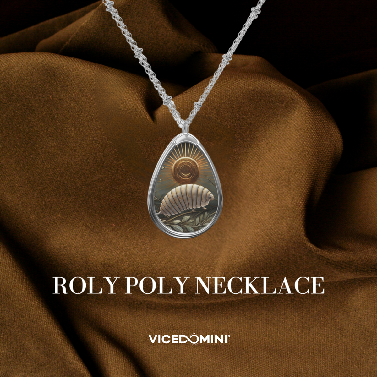 A teardrop-shaped pendant necklace on a silver chain, featuring a detailed illustration of a seashell and sun, displayed against draped brown satin fabric with text overlays reading 'ROLY POLY NECKLACE' and 'VICEDOMINI'.
