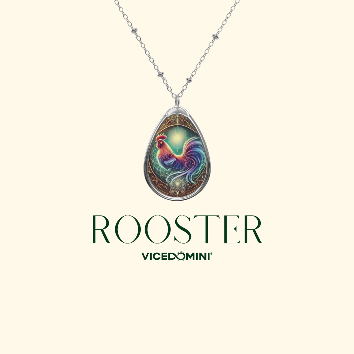 A rooster-themed teardrop pendant necklace is displayed on a plain beige background. The necklace has an ornate, celestial-inspired design, with a colorful rooster in the center. Below, the words "ROOSTER" and "VICEDOMINI" are written in elegant typography.