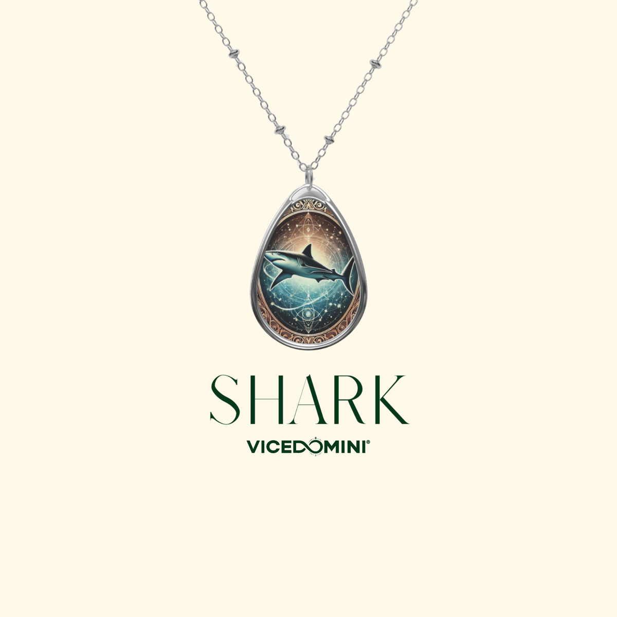 A minimalist product display featuring a silver shark pendant necklace against a light cream background. The pendant showcases a celestial-style shark surrounded by geometric patterns, with "SHARK" and "VICEDOMINI" text in elegant green typography.