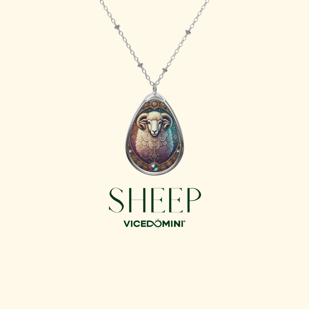 A silver necklace with a teardrop-shaped pendant showcasing an artistic sheep illustration. The background is soft beige with the text "SHEEP – VICEDOMINI" beneath it.