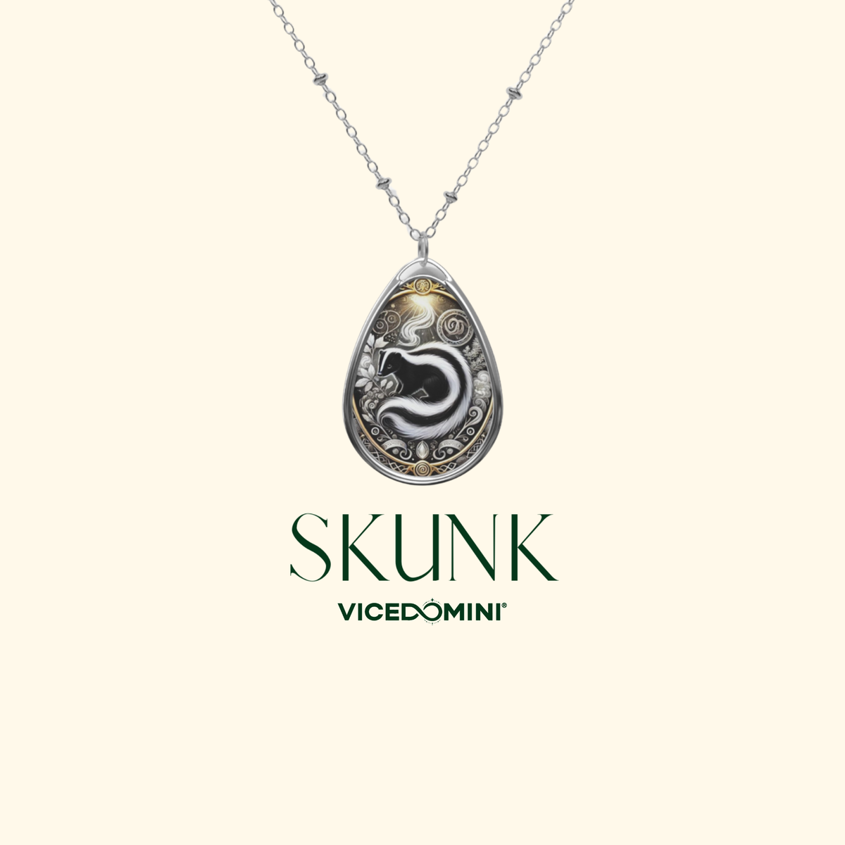 A silver-toned teardrop pendant necklace with an engraved black and white snake design and gold accents, suspended from a delicate silver chain. The brand name 'SKUNK' and sub-brand 'VICEDOMINI' are printed below the pendant on a solid pale cream background.