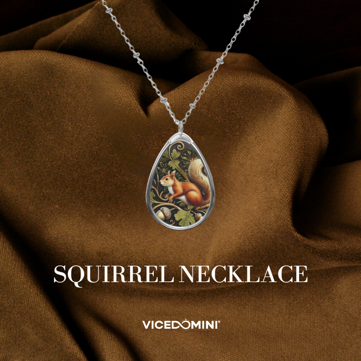 A teardrop-shaped silver pendant necklace featuring an illustrated squirrel on a tree branch, draped over brown satin fabric. The text 'SQUIRREL NECKLACE' and the brand 'VICEDOMINI' are displayed below.