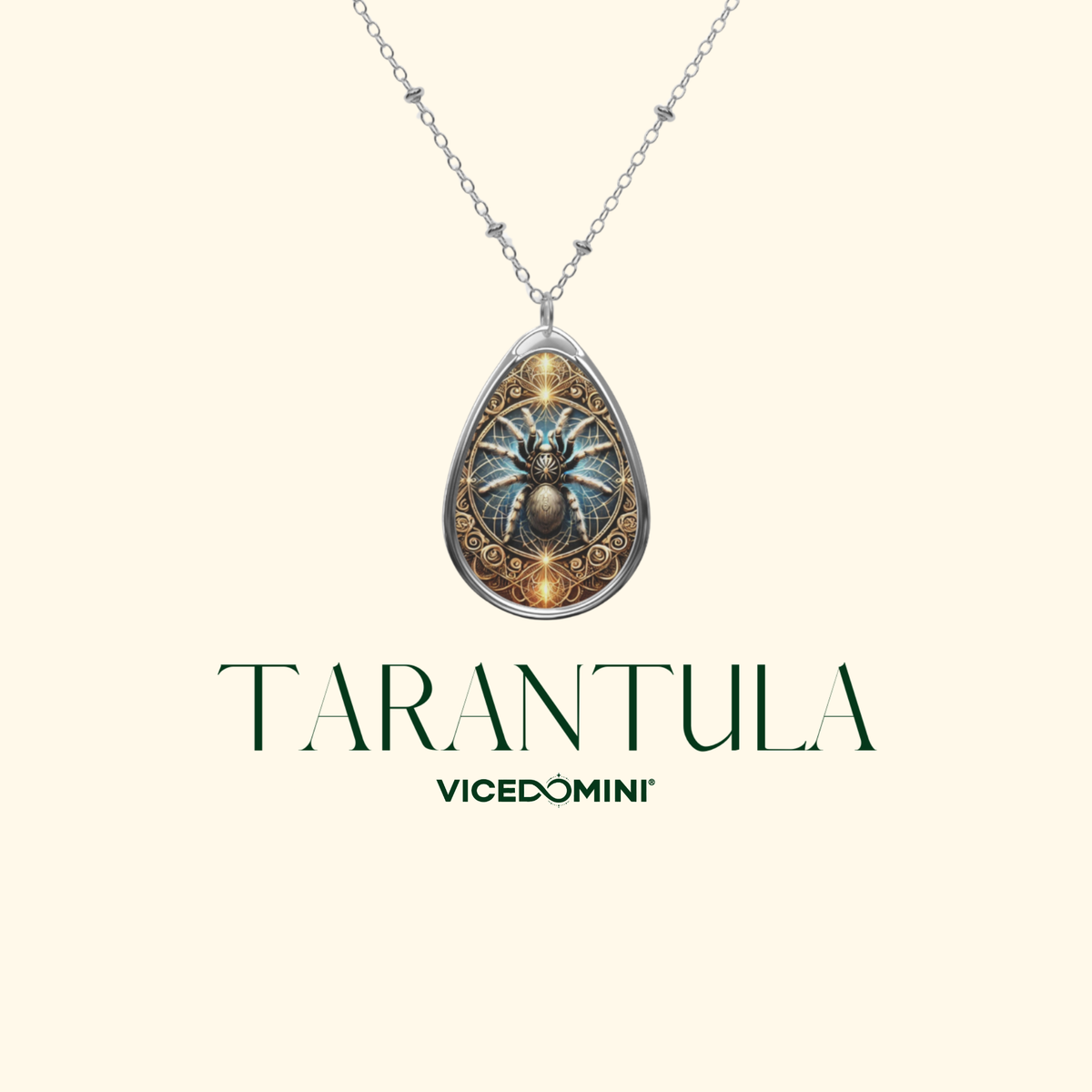 A teardrop-shaped pendant necklace featuring a highly detailed fantasy spider design with gold and blue tones, suspended from a silver-toned chain. The pendant is displayed against a solid cream background with the text 'TARANTULA' and 'VICEDOMINI' printed below.