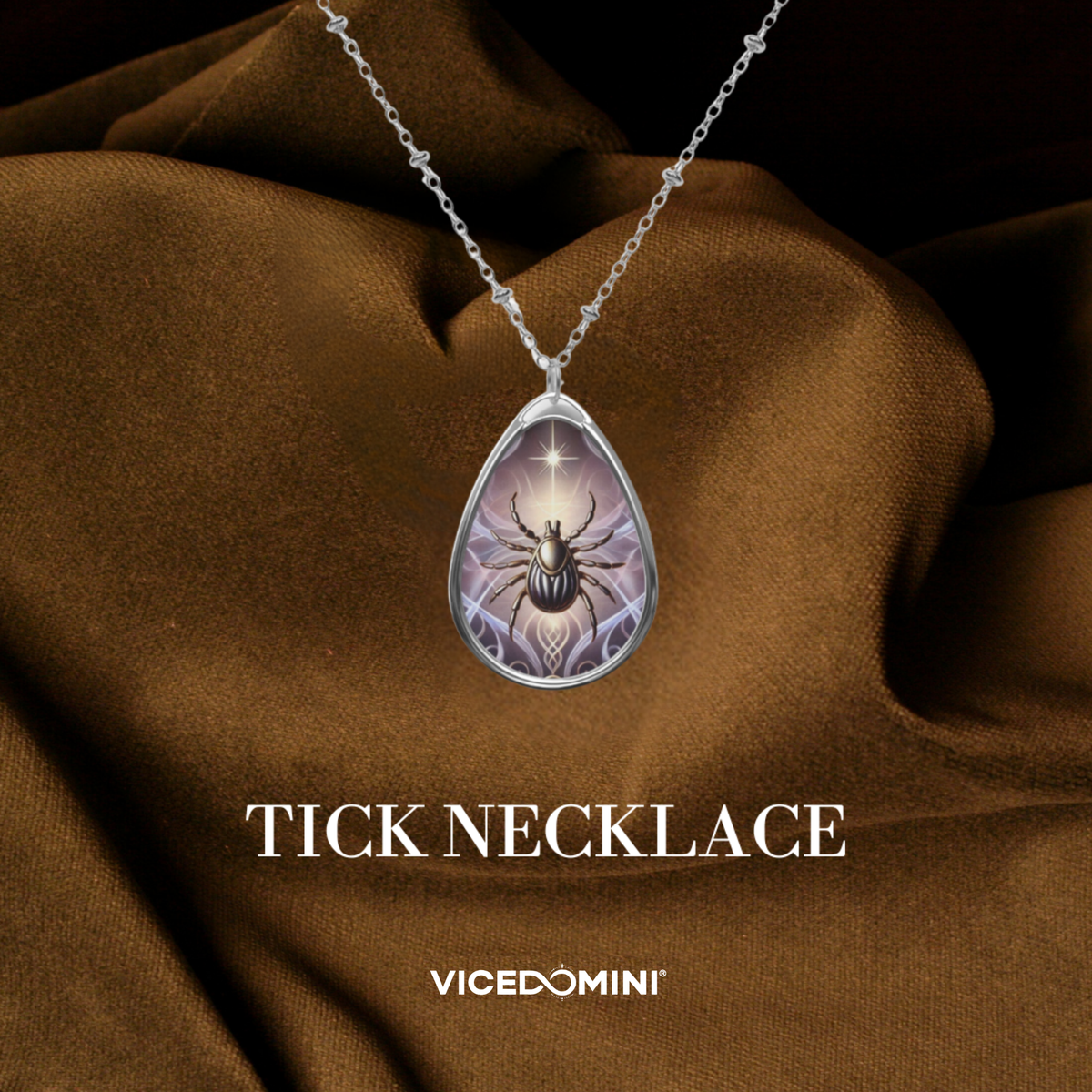 A teardrop-shaped pendant necklace featuring a silver-toned beetle illustration on a purple and white background, suspended from a silver chain. The necklace is displayed against a draped brown fabric backdrop with the text 'TICK NECKLACE' and the brand 'VICEDOMINI' below.