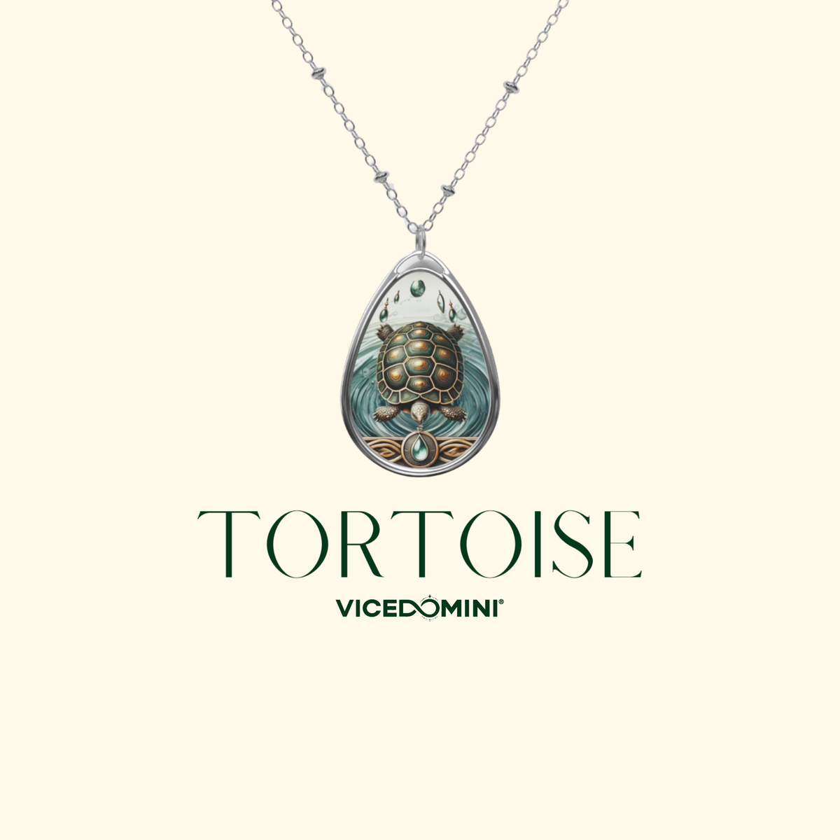 A teardrop pendant necklace featuring a detailed turtle illustration in muted teal, brown, and gold tones, suspended from a silver chain. The brand name 'TORTOISE' is displayed below the pendant, with 'VICEDOMINI' underneath, all on a solid pale cream background.