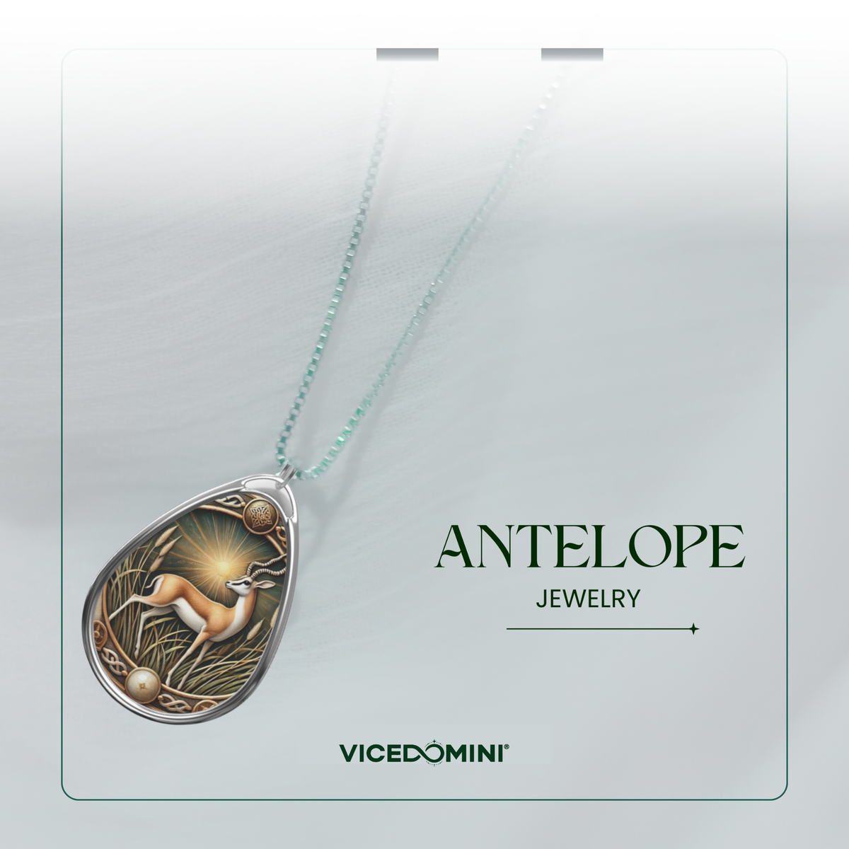 Teardrop-shaped pendant necklace on a fine chain, featuring a detailed antelope illustration with a glowing sunburst and natural textures. The pendant is displayed on a white card labeled 'ANTELOPE JEWELRY' and 'VICEDOMINI'.