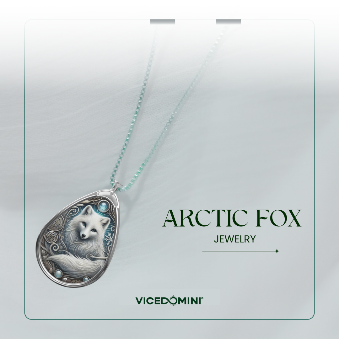 A teardrop-shaped pendant necklace featuring an engraved white arctic fox with blue accents, suspended from a light mint-green chain. The pendant is displayed on a white card labeled 'ARCTIC FOX JEWELRY' and 'VICEDOMINI'.
