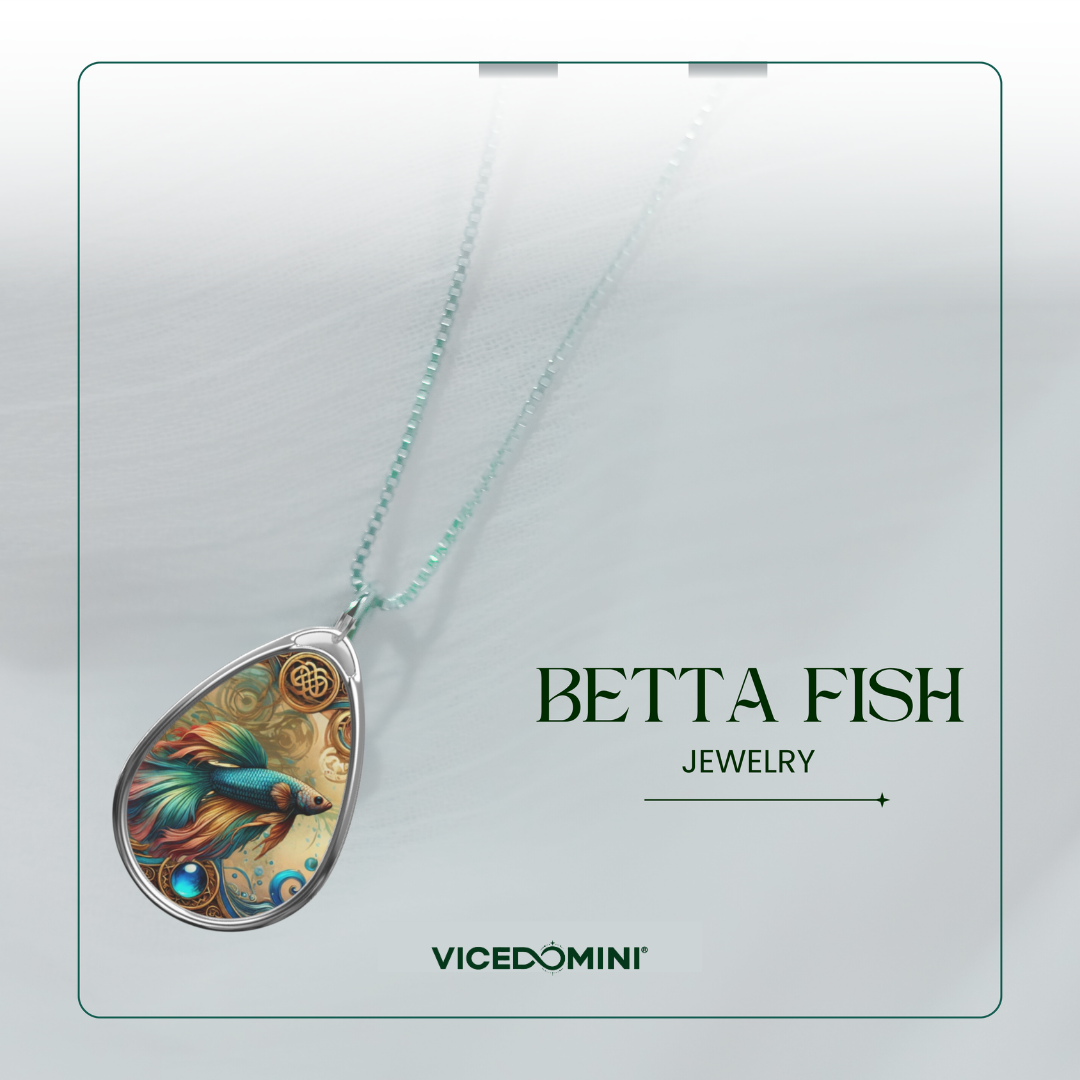 A teardrop-shaped pendant necklace featuring a colorful betta fish illustration with gold and blue tones, suspended from a light aqua chain. The pendant is displayed on a clean, light gray background with a thin green border, alongside the text 'BETTA FISH JEWELRY' and the brand name 'VICEDOMINI'.
