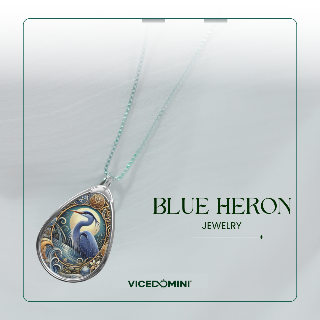 A teardrop pendant necklace featuring an intricate illustration of a blue heron with blue, gold, and white details, suspended from a light mint-green chain. The pendant is displayed on a light gray textured background with the text 'BLUE HERON JEWELRY' and the brand 'VICEDOMINI'.