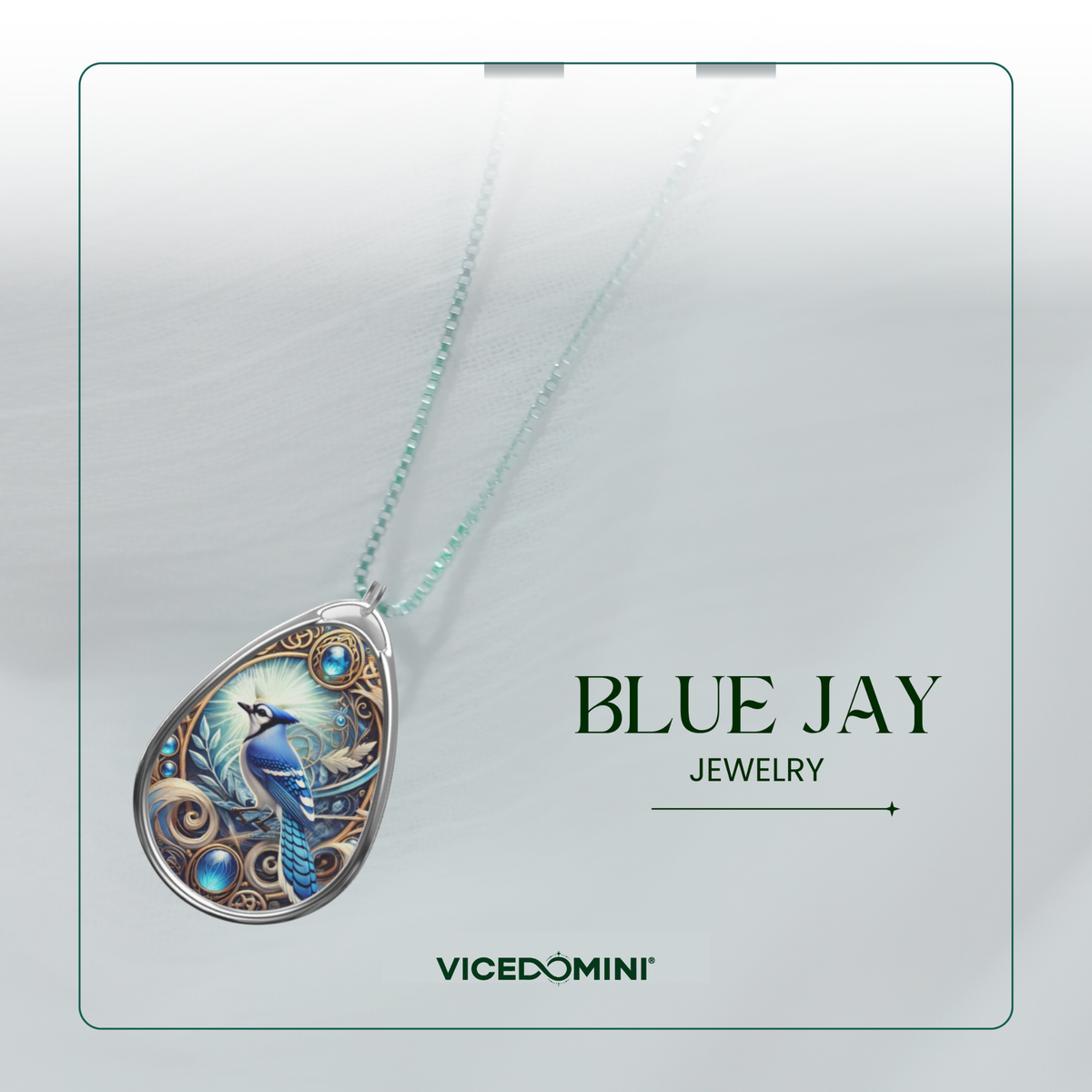 A teardrop-shaped pendant necklace from Vicedomini Blue Jay Jewelry, featuring a detailed blue bird illustration on a silver-toned frame with a light blue bead chain, displayed on a light gray textured background.