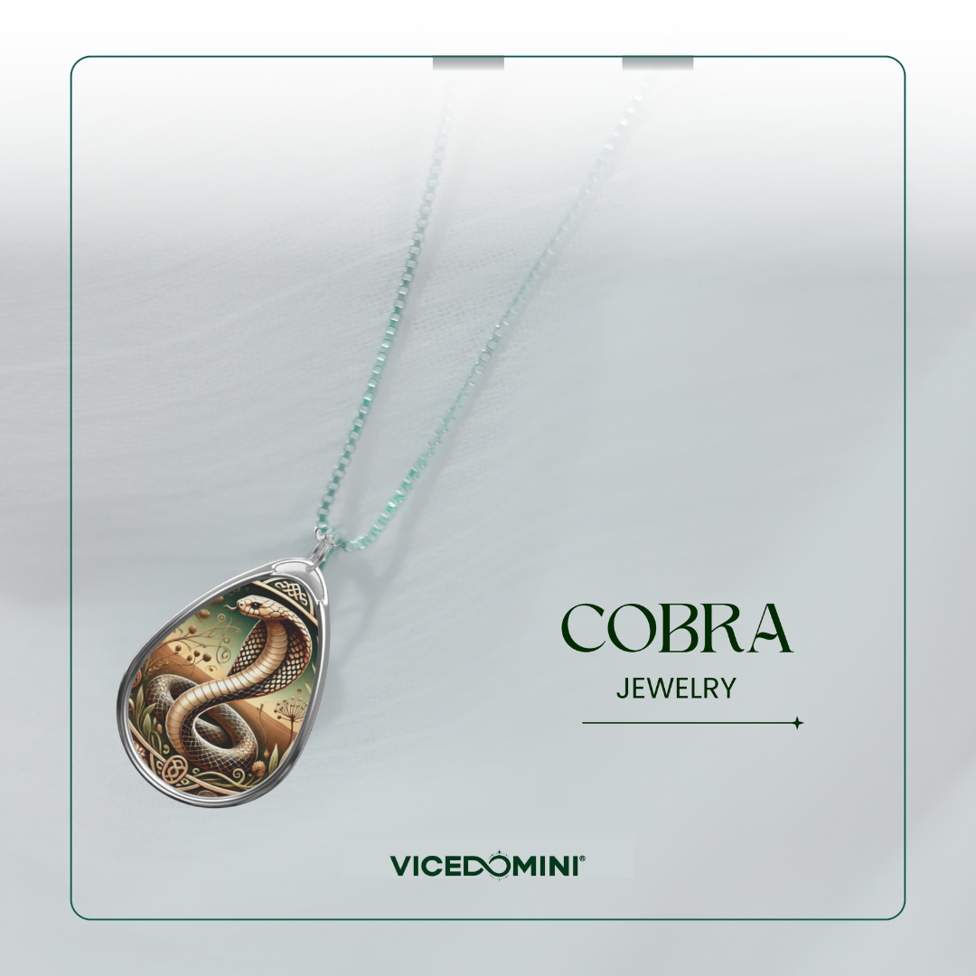 A teardrop-shaped pendant necklace featuring an intricate snake illustration, suspended from a delicate mint green chain. The pendant is displayed on a light gray background with a soft shadow, alongside the text 'COBRA JEWELRY' and the brand name 'VICEDOMINI'.