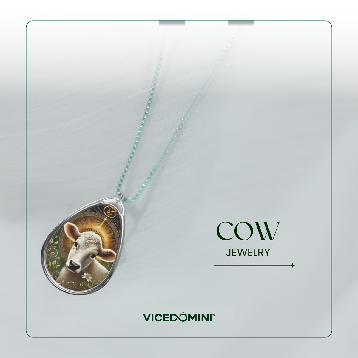 A teardrop-shaped pendant necklace featuring a detailed illustration of a cow with a gold halo, suspended from a delicate mint green chain. The pendant is displayed on a light gray background with a thin green border, alongside the text 'COW JEWELRY' and the brand name 'VICEDOMINI'.