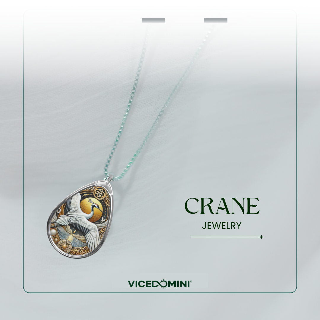 A teardrop-shaped pendant necklace from Vicedomini Crane Jewelry, featuring a detailed crane illustration in white, gold, and blue on a silver-toned frame, suspended from a light aqua chain against a soft gray background.