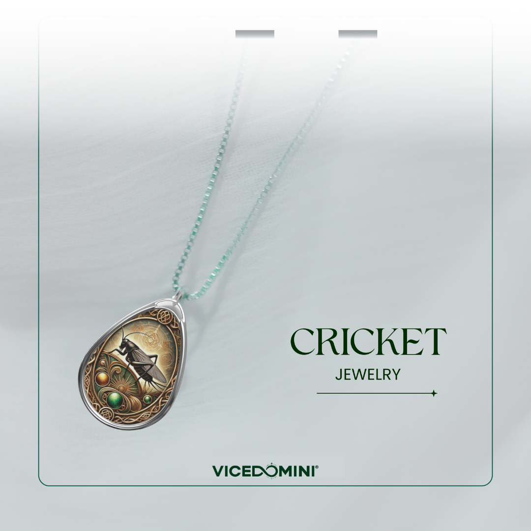 Teardrop-shaped pendant necklace on a light gray display card. The pendant has a silver-toned border and frame with a central gold-toned circular inset showing a black cricket in flight above green gemstone accents.