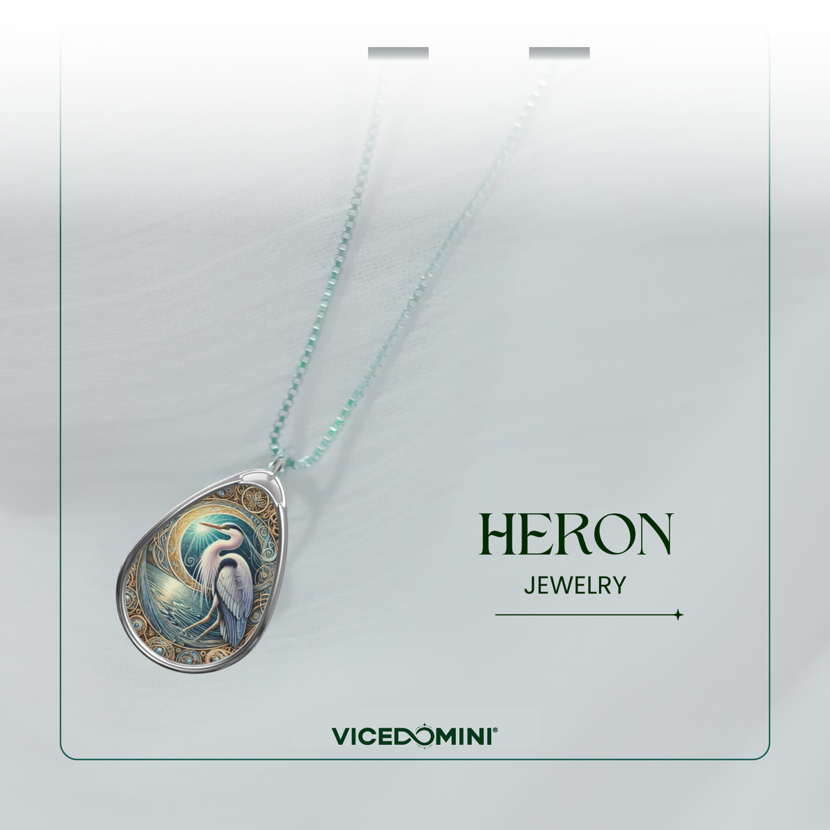A teardrop-shaped pendant necklace from Vicedomini Heron Jewelry, featuring a detailed fantasy illustration of a blue and white bird with gold accents, suspended on a delicate mint green chain against a light gray background.