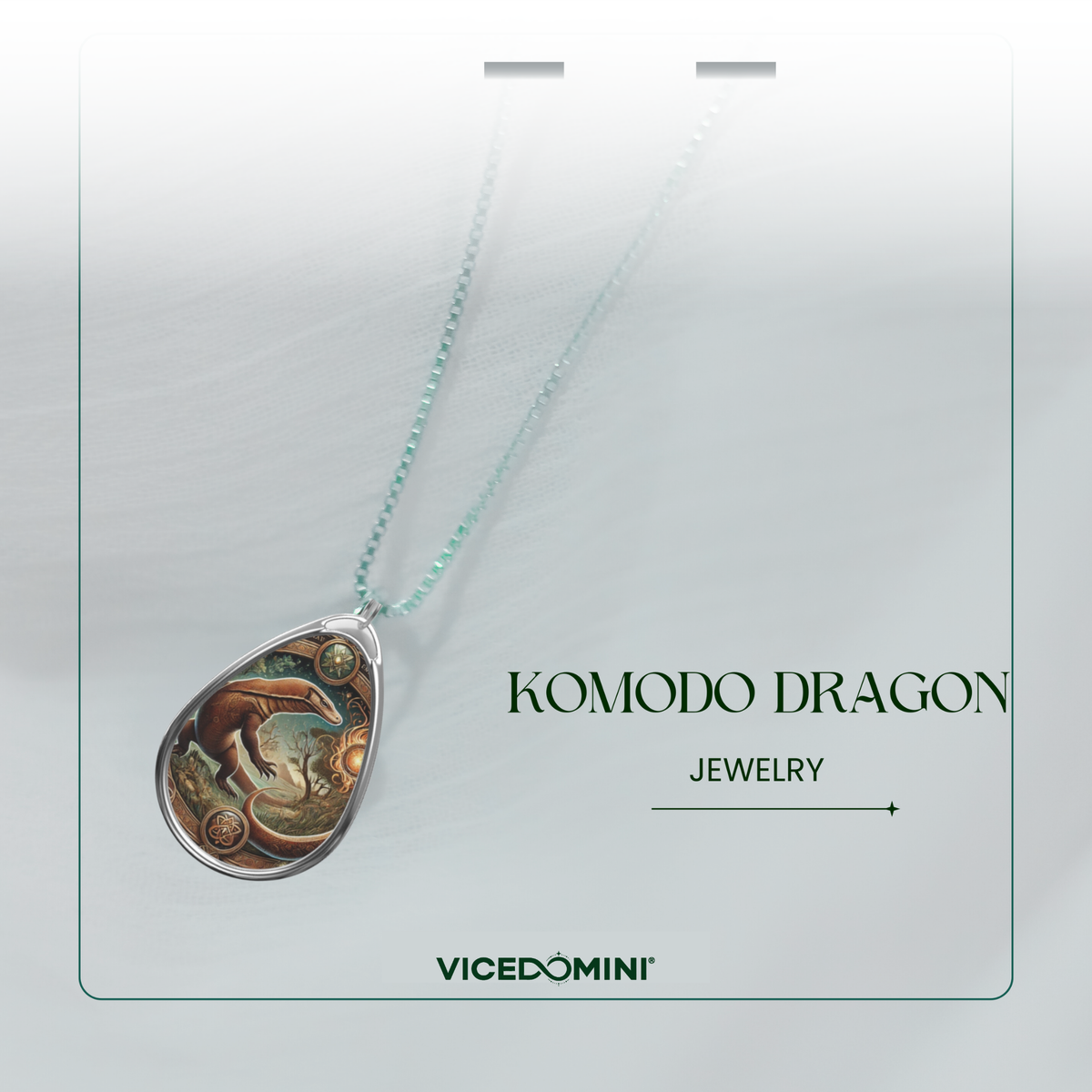 A teardrop-shaped pendant necklace featuring an illustrated Komodo dragon design, suspended from a delicate mint green chain. The pendant is displayed on a white card with the text 'KOMODO DRAGON JEWELRY' and the brand 'VICEDOMINI'.