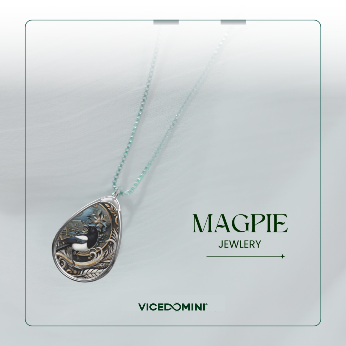 A teardrop-shaped pendant necklace with a silver-toned frame, featuring a detailed black bird illustration over a blue-gray background, hanging on a delicate mint-green chain. The image is presented on a light gray textured card with the brand names 'MAGPIE JEWLERY' and 'VICEDOMINI' printed on the right.