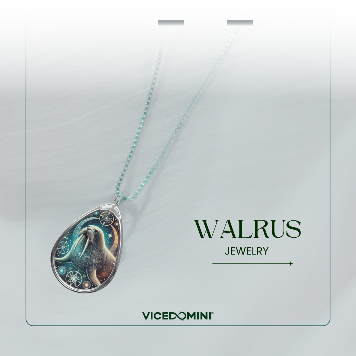 A refined product shot of the walrus necklace, elegantly draped over a soft, light-colored fabric with a subtle green-tinted chain. The pendant’s celestial walrus design shines under soft lighting, with the logo 'vicedomini' displayed below.