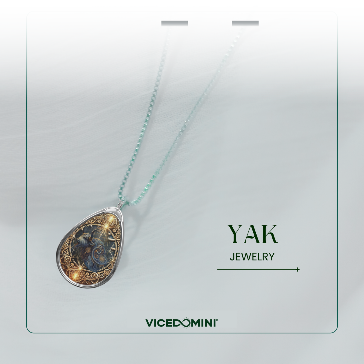 A teardrop-shaped pendant necklace with a silver-toned frame and a detailed blue and gold illustration, hanging from a light aqua chain on a white display card. The card features the text 'YAK JEWELRY' and the brand 'VICEDOMINI'.