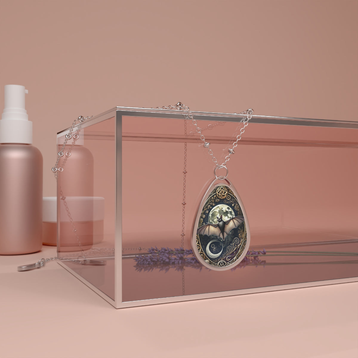 A silver necklace featuring a bat pendant draped over a transparent box with lavender sprigs and cosmetics in the background, set against a soft pink backdrop. The pendant shows a bat flying in front of a full moon, surrounded by intricate patterns and celestial symbols, giving it a mystical appearance.